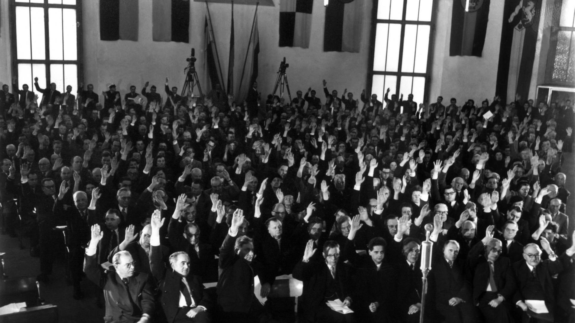 Die Teilnehmer erteilen durch Handzeichen ihre Zustimmung zum Deutschen Manifest. Der historische Saal der Frankfurter Paulskirche war am 29.01.1955 während der Protestkundgebung mit den Flaggen aller deutschen Länder geschmückt. Auf Initiative der SPD und des Deutschen Gewerkschaftsbundes (DGB) hatten sich Persönlichkeiten des öffentlichen Lebens eingefunden, um gegen die Ratifizierung der Pariser Verträge zu protestieren. Zum Schluss der Kundgebung nahmen sie einstimmig ein Manifest ("Deutsches Manifest") an, in dem Volk und Regierung zum Widerstand gegen die sich immer stärker werdende Tendenz zur Spaltung Deutschland aufgerufen wurden. Die Teilnehmer erteilen durch Handzeichen ihre Zustimmung zum Deutschen Manifest. Der historische Saal der Frankfurter Paulskirche war am 29.01.1955 während der Protestkundgebung mit den Flaggen aller deutschen Länder geschmückt. Auf Initiative der SPD und des Deutschen Gewerkschaftsbundes (DGB) hatten sich Persönlichkeiten des öffentlichen Lebens eingefunden, um gegen die Ratifizierung der Pariser Verträge zu protestieren. Zum Schluss der Kundgebung nahmen sie einstimmig ein Manifest ("Deutsches Manifest") an, in dem Volk und Regierung zum Widerstand gegen die sich immer stärker werdende Tendenz zur Spaltung Deutschland aufgerufen wurden.