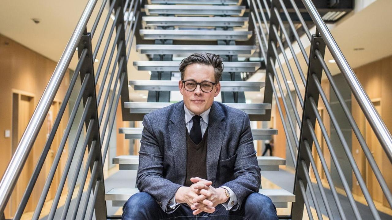 Konstantin von Notz, mit Brille im grauen Anzug, sitzt auf einer Treppe im Lichthof eines mehrstöckigen Gebäudes. Konstantin von Notz, mit Brille im grauen Anzug, sitzt auf einer Treppe im Lichthof eines mehrstöckigen Gebäudes.