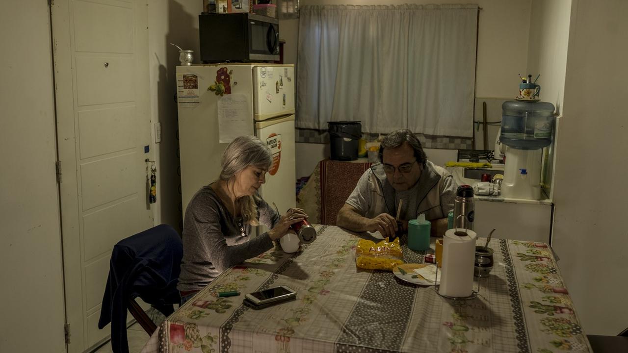 Ein älteres Paar sitzt in der Küche an einem Tisch. Im Hintergrund steht ein großer Kühlschrank. Ein älteres Paar sitzt in der Küche an einem Tisch. Im Hintergrund steht ein großer Kühlschrank.