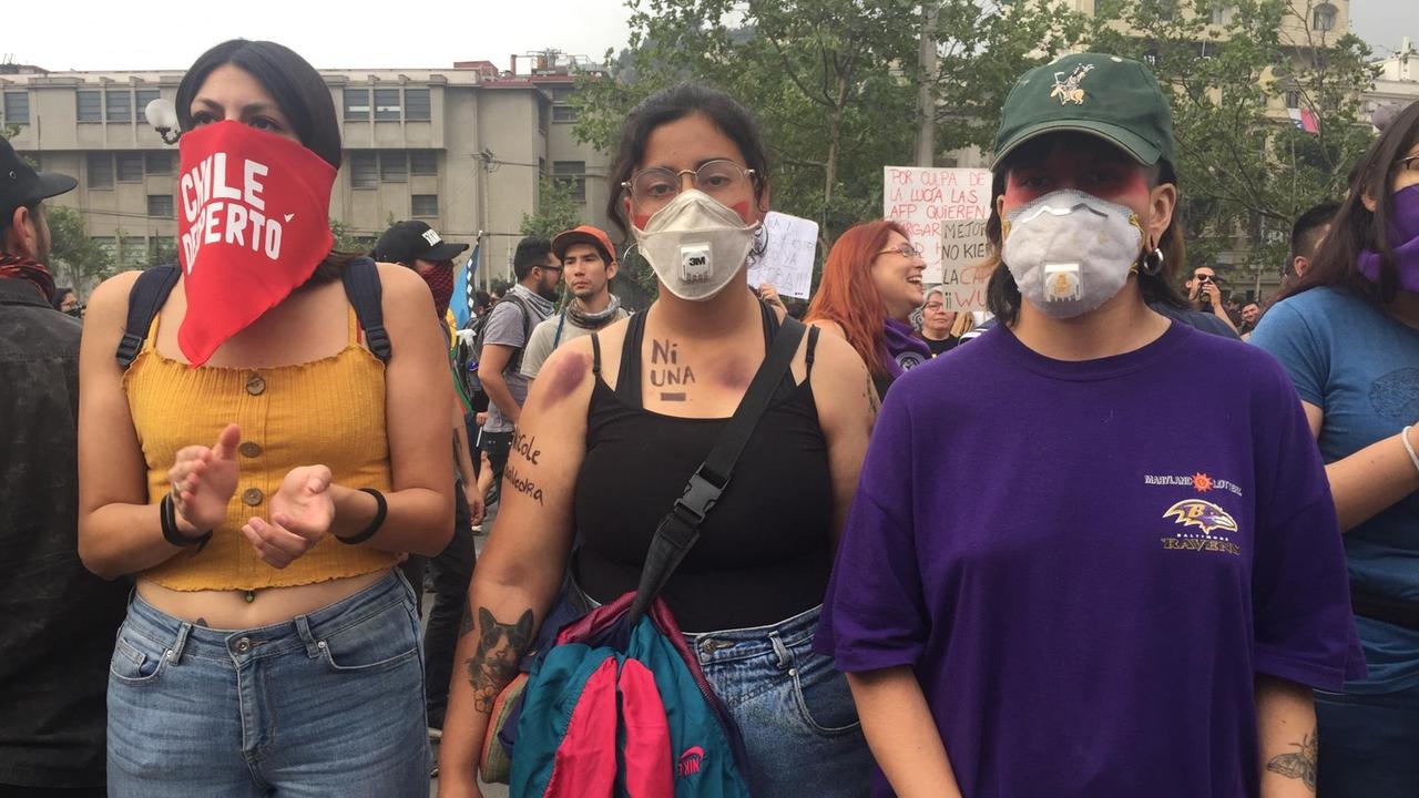 Drei junge Demonstrantinnen in Santiago de Chile, die sich durch Mundschutz vor dem Tränengas schützen. Drei junge Demonstrantinnen in Santiago de Chile, die sich durch Mundschutz vor dem Tränengas schützen.