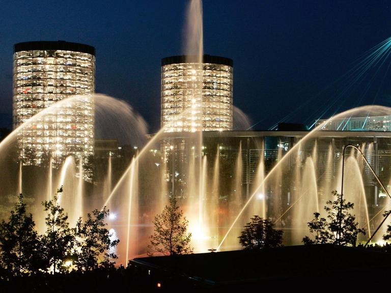 Licht- und Wasserspiele vor dunkelblauem Nachthimmel und zwei beleuchteten Hochhäusern in der Autostadt Wolfsburg