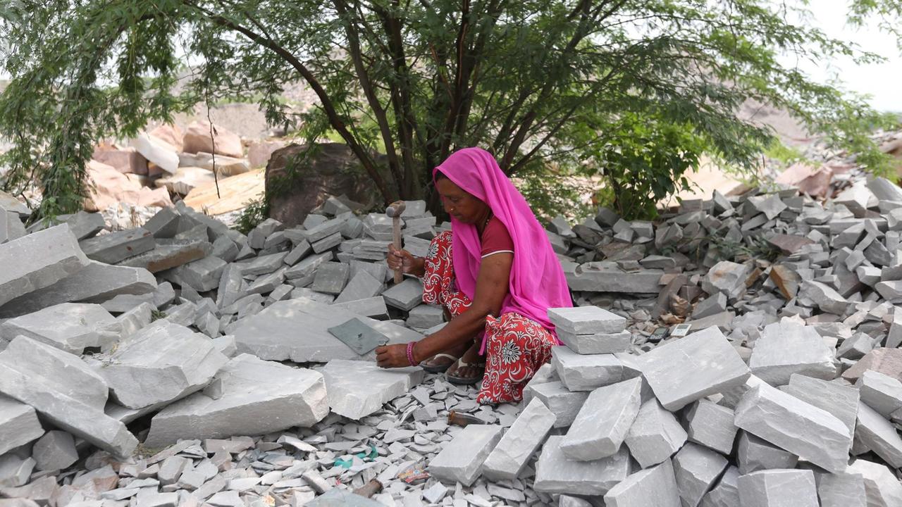 Eine Frau in einer Steinmine hockt und bearbeitet einen Stein.