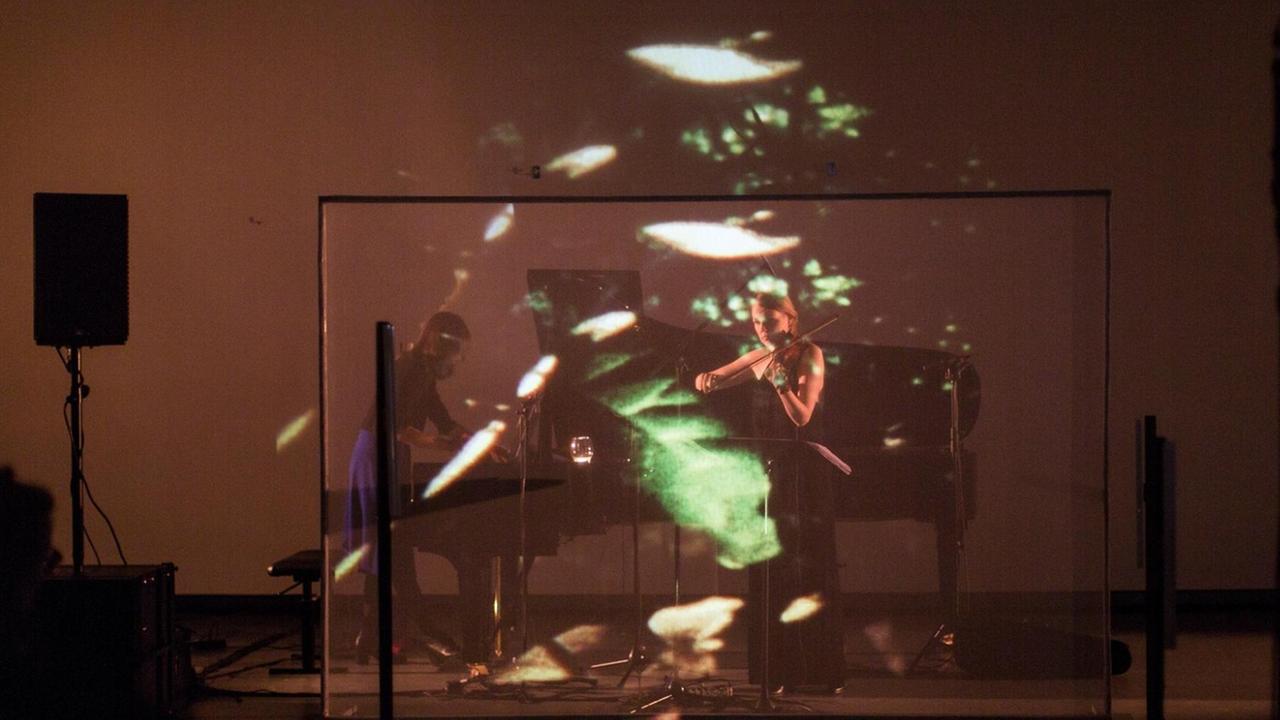 Das Duo Hellqvist/Amaral auf der Bühne mit Lichtreflexen auf einem Gaze-Vorhang Das Duo Hellqvist/Amaral auf der Bühne mit Lichtreflexen auf einem Gaze-Vorhang