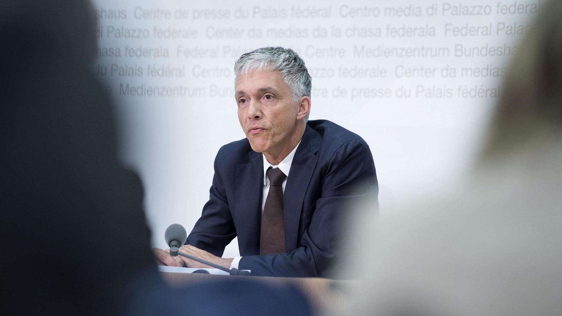Foto vom oberste Strafermittler der Schweiz, Michael Lauber, bei einer Pressekonferenz durch zwei Journalisten hindurch Foto vom oberste Strafermittler der Schweiz, Michael Lauber, bei einer Pressekonferenz durch zwei Journalisten hindurch