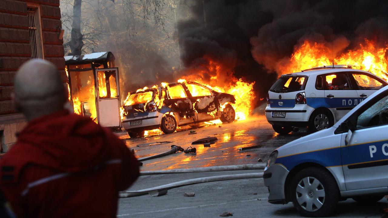 Dunkler Rauch steigt über brennenden Polizeiautos in Sarajevo auf. Dunkler Rauch steigt über brennenden Polizeiautos in Sarajevo auf.