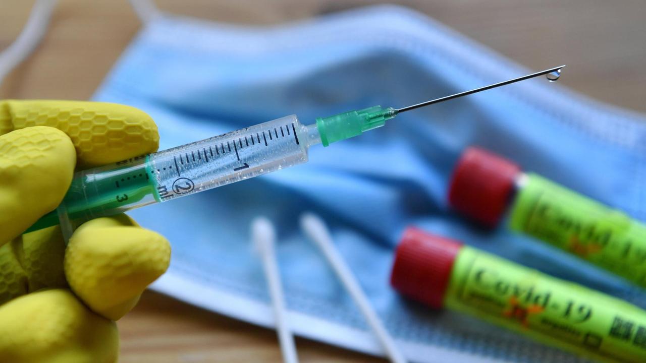 Eine Hand in Gummihandschuhe gehüllt hält eine Einwegspritze mit Impfstoff zur Injektion mit einer Kanüle - Symbolbild Corona-Impfstoff