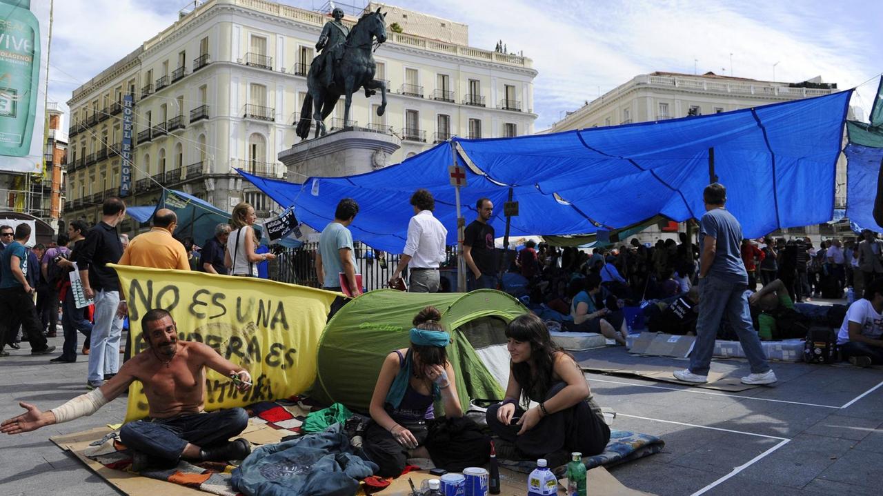 Spanische Demonstranten sitzen vor ihren Zelten auf dem vollen Platz Puerta da Sol in Madrid.
