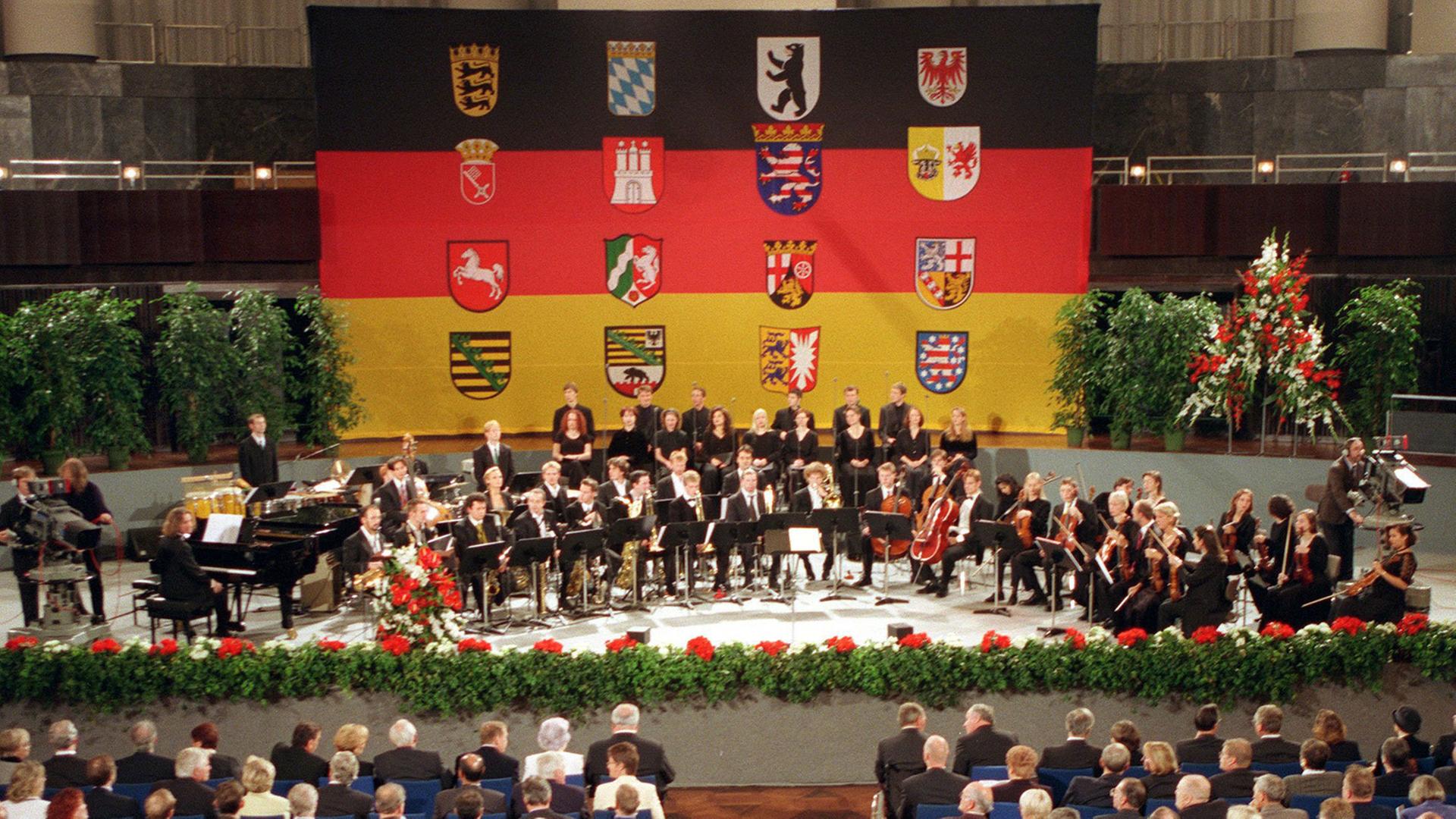 Zum Festakt am Tag der Deutschen Einheit sind am 3.10.1998 in Hannovers Kuppelsaal deutsche Spitzenpolitiker sowie Gäste aus dem In- und Ausland gekommen, die Bühne ist mit den Wappen der 16 Bundesländer geschmückt. Zum Auftakt des Festaktes wurde das umstrittene Musikstück mit Teilen der ehemaligen DDR-Hymne uraufgeführt, um das es im Vorfeld der Einheitsfeiern wochenlang Streit gegeben hatte. Die bayerische Staatsregierung hatte ihre Teilnahme an den Einheitsfeiern aus Protest gegen das Werk abgesagt. Zum Festakt am Tag der Deutschen Einheit sind am 3.10.1998 in Hannovers Kuppelsaal deutsche Spitzenpolitiker sowie Gäste aus dem In- und Ausland gekommen, die Bühne ist mit den Wappen der 16 Bundesländer geschmückt. Zum Auftakt des Festaktes wurde das umstrittene Musikstück mit Teilen der ehemaligen DDR-Hymne uraufgeführt, um das es im Vorfeld der Einheitsfeiern wochenlang Streit gegeben hatte. Die bayerische Staatsregierung hatte ihre Teilnahme an den Einheitsfeiern aus Protest gegen das Werk abgesagt.