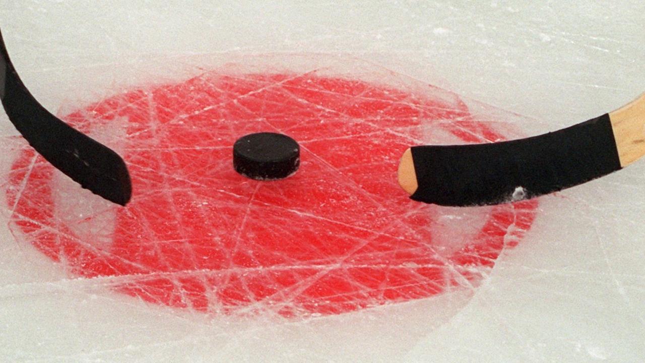Zwei Eishockeyschläger liegen an einem Puck Zwei Eishockeyschläger liegen an einem Puck