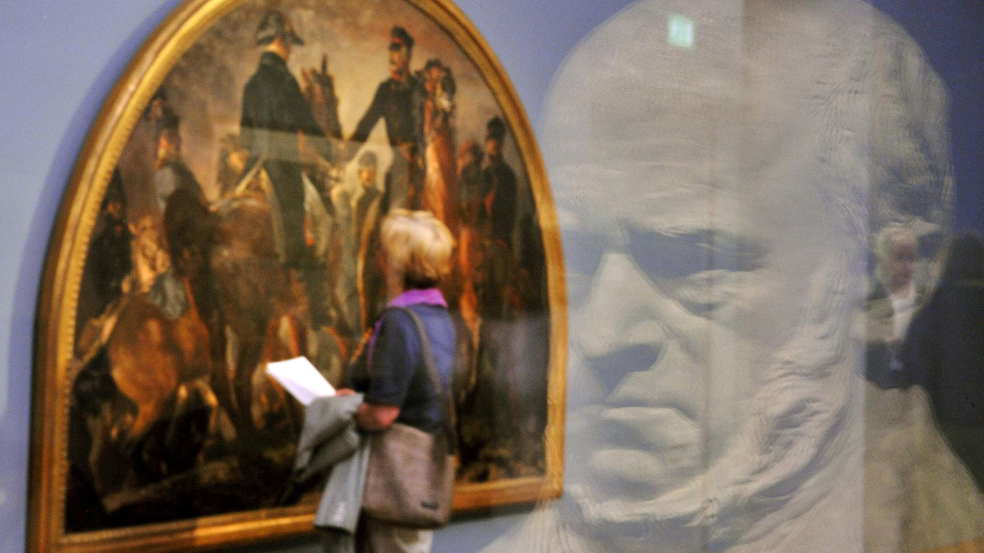 Eine Besucherin schaut sich das Gemälde "Blüchers Begegnung mit Wellington nach der Schlacht bei Belle-Alliance, 1858" von Adolph Menzel an. Im Vordergrund spiegelt sich die Gipsbüste Menzels, geschaffen von Reinhold Begas, in einer Glasscheibe. Eine Besucherin schaut sich das Gemälde "Blüchers Begegnung mit Wellington nach der Schlacht bei Belle-Alliance, 1858" von Adolph Menzel an. Im Vordergrund spiegelt sich die Gipsbüste Menzels, geschaffen von Reinhold Begas, in einer Glasscheibe.