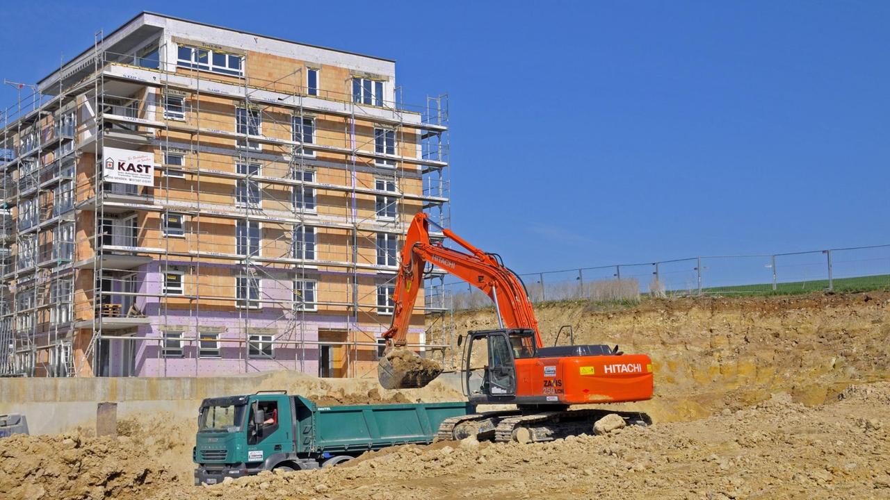 Ein Bagger hebt in Ulm in Baden-Württemberg eine Baugrube aus. Im Hintergrund ist ein Mehrfamilienhaus im Rohbau zu sehen. Ein Bagger hebt in Ulm in Baden-Württemberg eine Baugrube aus. Im Hintergrund ist ein Mehrfamilienhaus im Rohbau zu sehen.