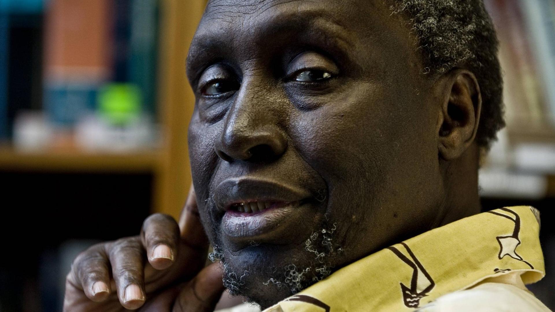 Portrait des kenianischen Schriftstellers Ngugi Wa Thiong o, der nach linke in die Kamera guckt und die rechte Hand mit Daumen und Zeigefinger an die Wange hält. Portrait des kenianischen Schriftstellers Ngugi Wa Thiong o, der nach linke in die Kamera guckt und die rechte Hand mit Daumen und Zeigefinger an die Wange hält.