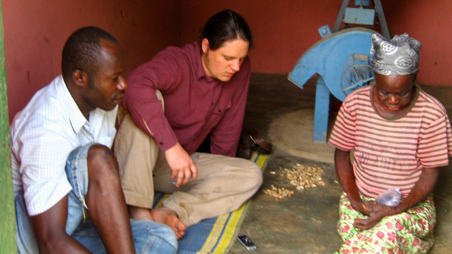 Ethnologe Felix Riedel mit Partnern in Nord-Ghana. Er sitzt auf dem Boden in einem Haus mit zwei anderen Männern.