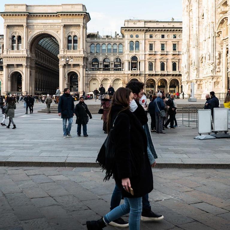 Menschen mit Mundschutz-Masken laufen im Zentrum Mailands über die Straße
