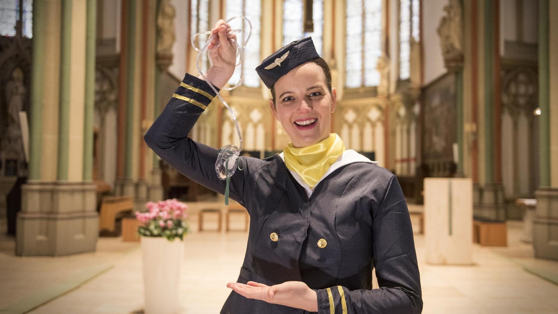 Eine Stewardess steht in einem Kirchenschiff und hält eine Sauerstoffmaskein die Höhe. Eine Stewardess steht in einem Kirchenschiff und hält eine Sauerstoffmaskein die Höhe.