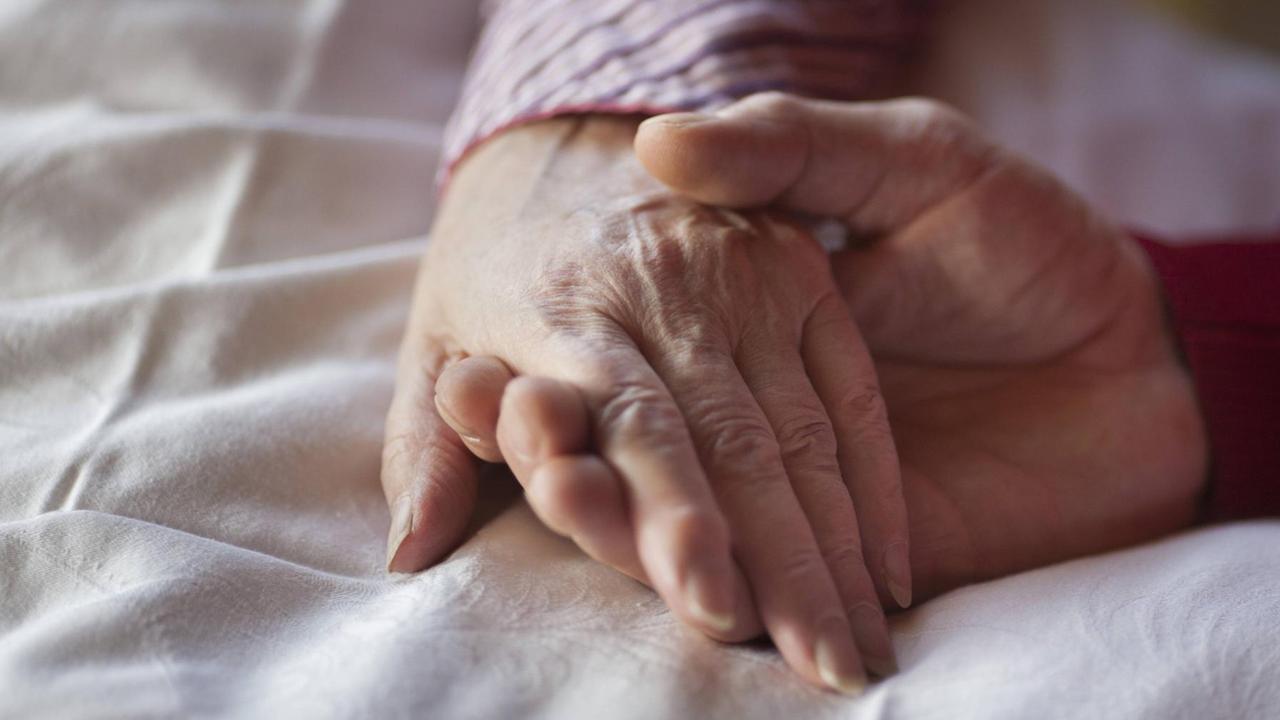 Ein Hospiz in Offenburg. An einem Bett wird von einer Person die Hand von einer anderen Person gehalten. Ein Hospiz in Offenburg. An einem Bett wird von einer Person die Hand von einer anderen Person gehalten.