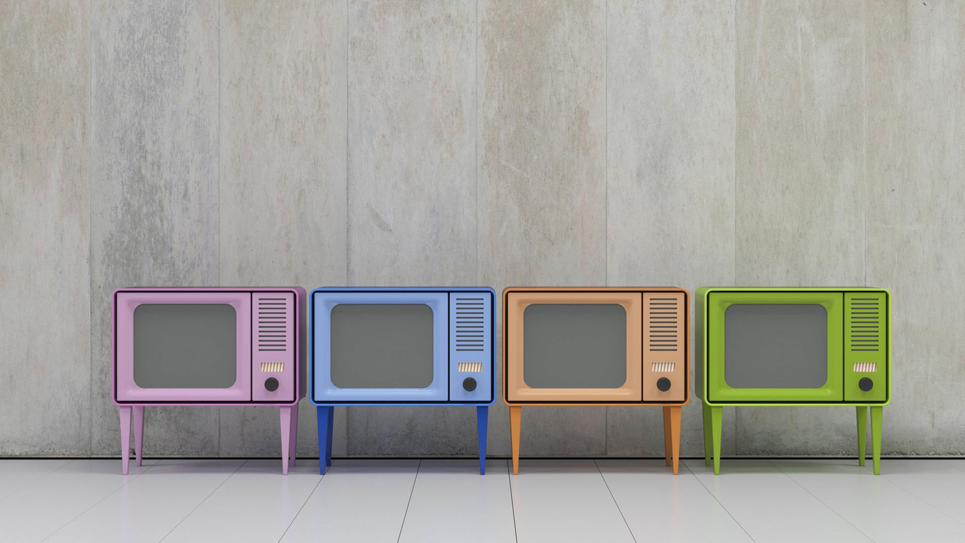 Das Bild zeigt vier Fernsehgeräte in vier verschiedenen Farben vor einer grauen Wand.