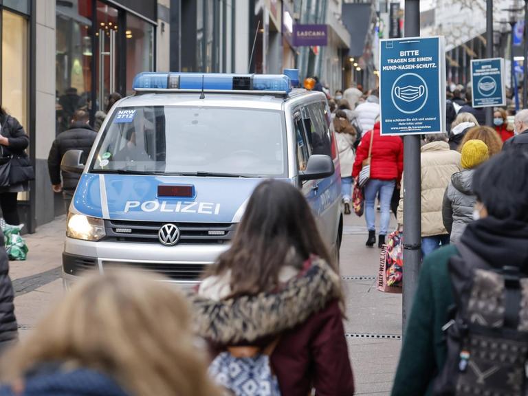 Passanten mit Schutzmasken beim Einkauf im Zentrum der Stadt Essen, links ein Polizeifahrzeug.
