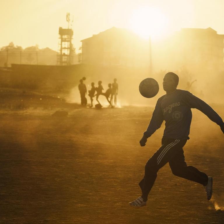 Jugendliche spielen im warmen abendlichen Gegenlicht Fußball in einem Slum Nairobis.