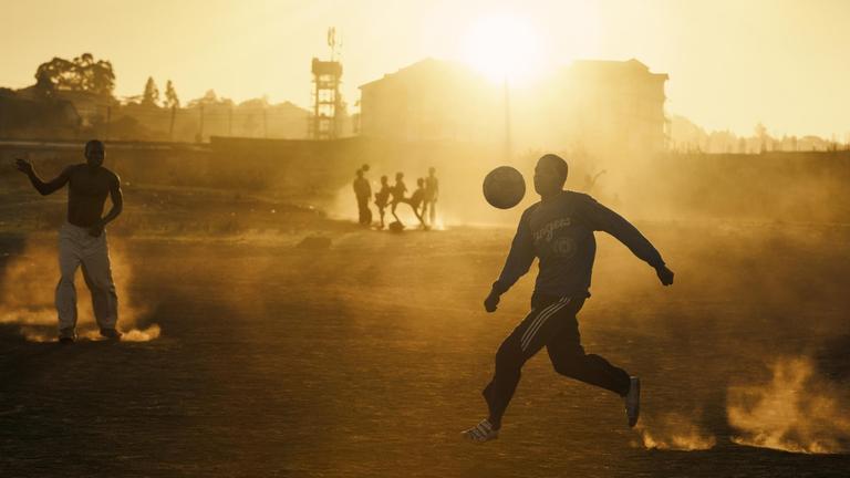 Jugendliche spielen im warmen abendlichen Gegenlicht Fußball in einem Slum Nairobis. Jugendliche spielen im warmen abendlichen Gegenlicht Fußball in einem Slum Nairobis.