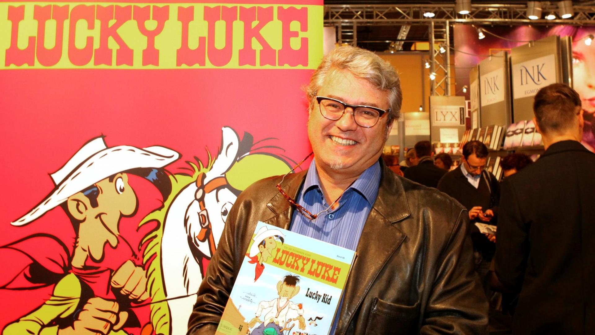 Der Lucky Luke Zeichner Achdé vor einem Plakat mit Lucky Luke. Der Lucky Luke Zeichner Achdé vor einem Plakat mit Lucky Luke.