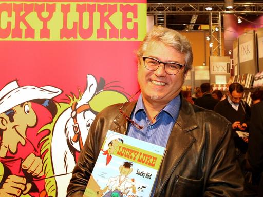 Der Lucky Luke Zeichner Achdé vor einem Plakat mit Lucky Luke.