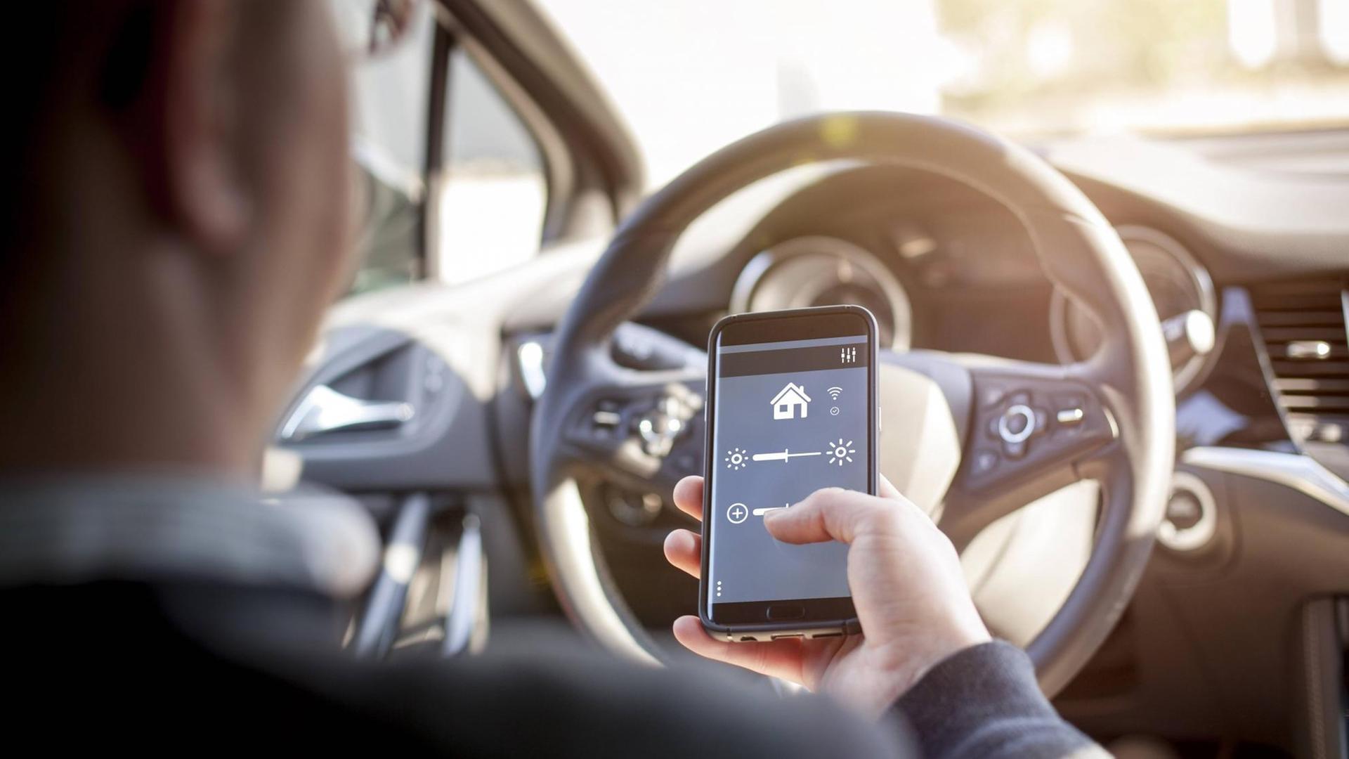 Ein Mann sitzt in einem Auto und steuert mit einem Smartphone die Einstellungen des Fahrzeugs.