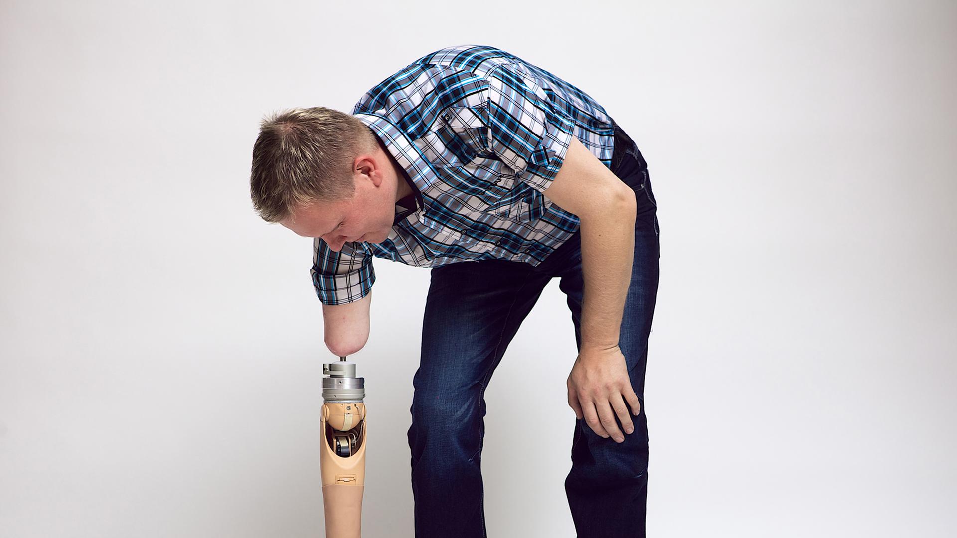 Ein Mann hebt mit einer Armprothese einen Ball vom Boden auf. Ein Mann hebt mit einer Armprothese einen Ball vom Boden auf.