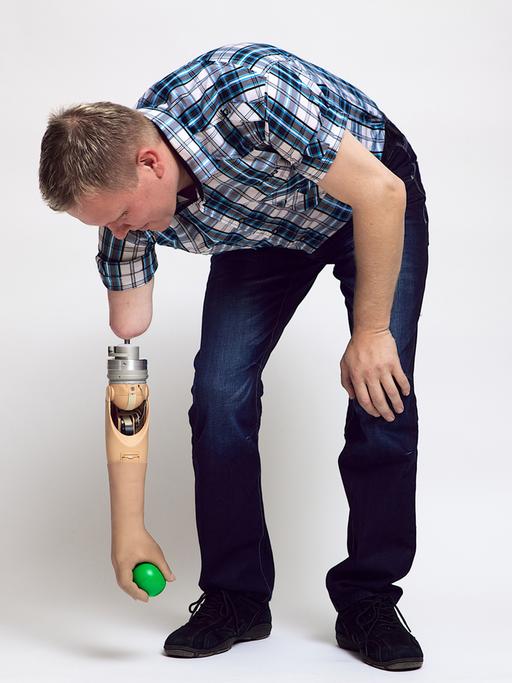 Ein Mann hebt mit einer Armprothese einen Ball vom Boden auf.