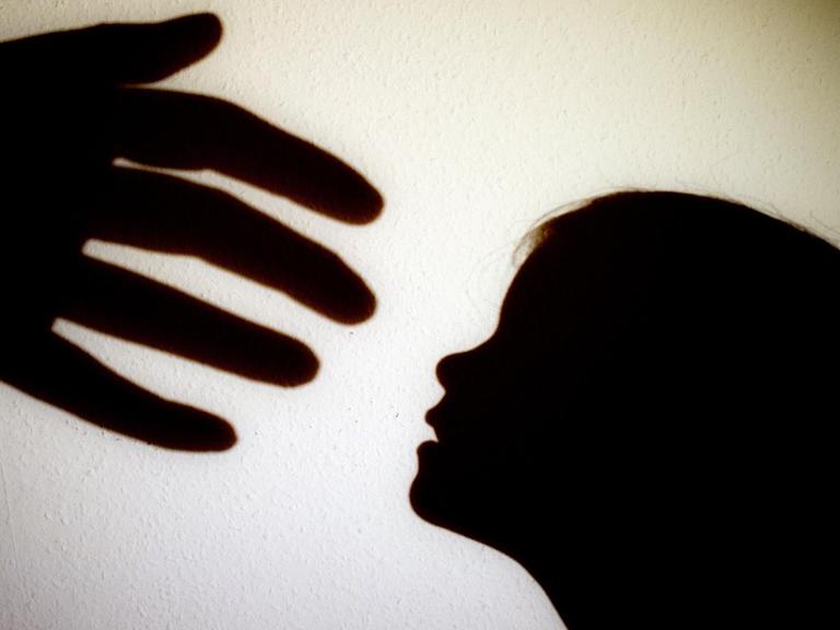 Schatten einer Hand einer erwachsenen Person und der Kopf eines Kindes an einer Wand eines Zimmers.