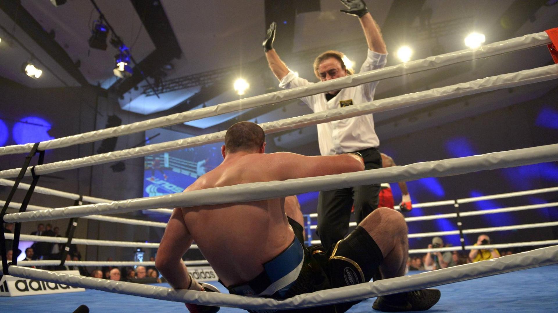 Ein Boxer sitzt am Boxring, er wird vom Ringrichter für kampfunfähig erklärt.