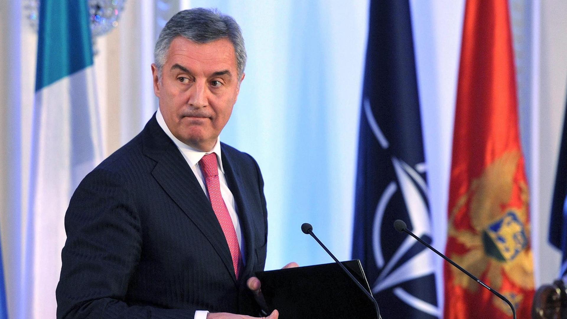 Milo Djukanovic steht an einem Rednerpult und schaut skeptisch zur Seite. Im Hintergrund sind Fahnen zu sehen. Milo Djukanovic steht an einem Rednerpult und schaut skeptisch zur Seite. Im Hintergrund sind Fahnen zu sehen.
