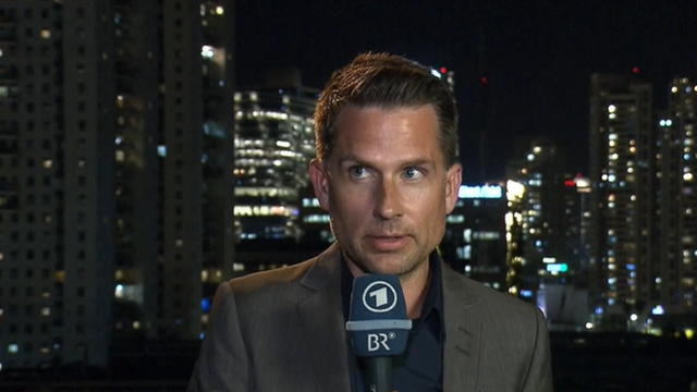 ARD-Korrespondent Mike Lingenfelser mit Mikrofon vor einem Nacht-Panorama Tel Avivs