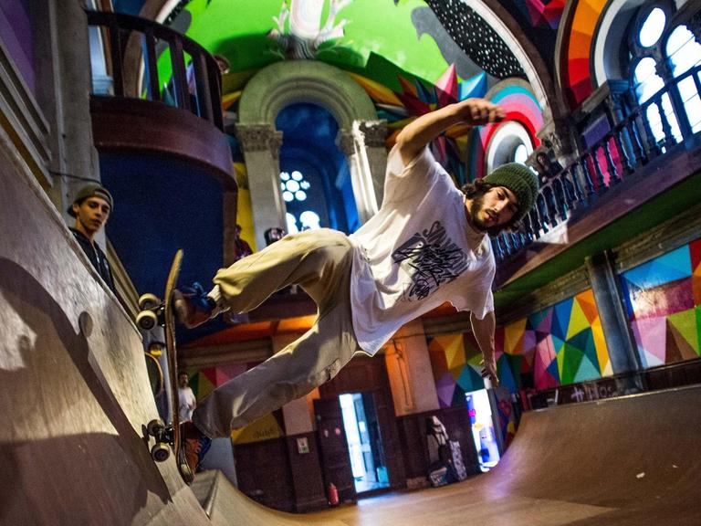 Eine leere Kirche beherbergt eine bunte Skaterbahn. Das Licht fällt durch die Kirchenfenster auf den Skater.