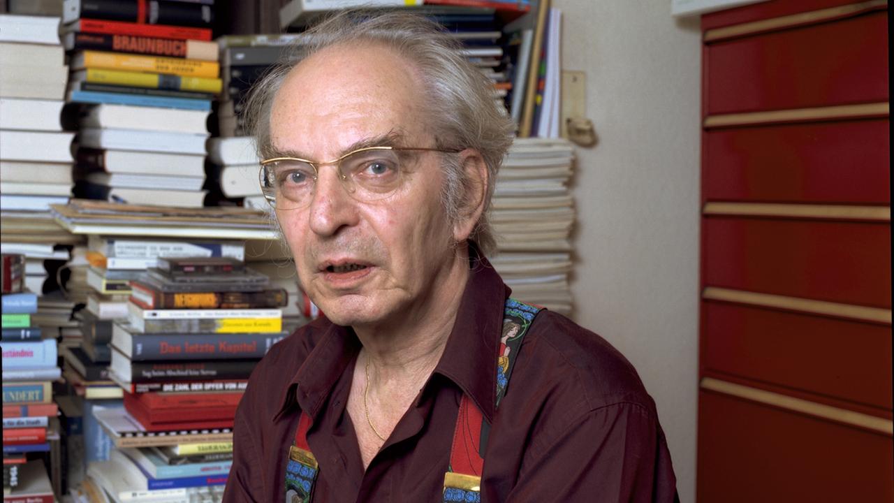 Hans G Helms steht mit seinem roten Hemd und seinen bunten Hosenträgern vor seinem Bücherregal. Hans G Helms steht mit seinem roten Hemd und seinen bunten Hosenträgern vor seinem Bücherregal.