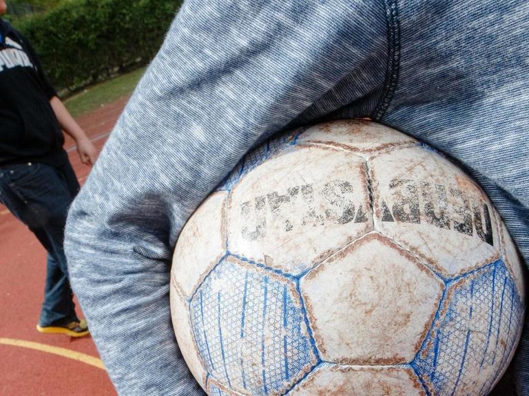 Ein Junge hält am 07.05.2015 in Hamburg auf einem Bolzplatz einen Fußball unter dem Arm.