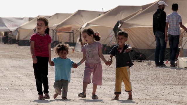 Vier Kinder, 2 größere Mädchen und 2 kleinere Jungs, gehen Hand in Hand auf einem Weg im Flüchtlingslager, im Hintergrund sind Zelte zu sehen Vier Kinder, 2 größere Mädchen und 2 kleinere Jungs, gehen Hand in Hand auf einem Weg im Flüchtlingslager, im Hintergrund sind Zelte zu sehen