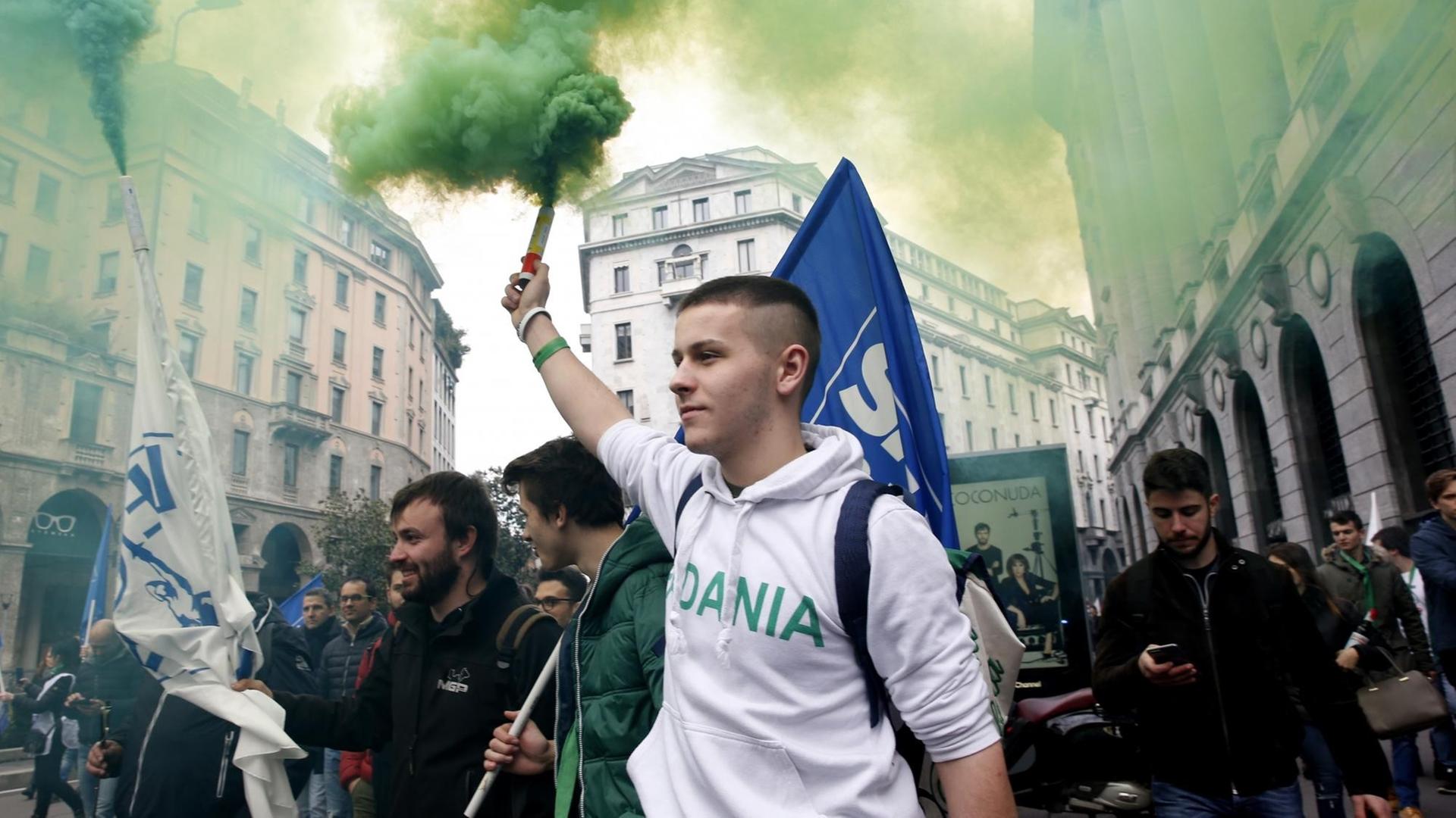 Ein junger Mann im Kapuzenpulli, ein Aktivist der rechtspopulistischen Partei Lega, hält bei einer Demonstration eine Rauchfackel in die Höhe. Im Hintgergrund Flaggen, Rauch und weitere Demonstranten. Ein junger Mann im Kapuzenpulli, ein Aktivist der rechtspopulistischen Partei Lega, hält bei einer Demonstration eine Rauchfackel in die Höhe. Im Hintgergrund Flaggen, Rauch und weitere Demonstranten.