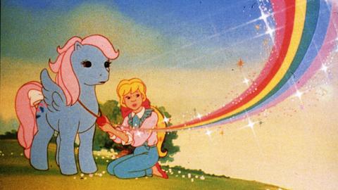 Zeichentrickszene: Neben einem blauen Pony sitzt ein blondes Mädchen. Im Hintergrund ist ein Regenbogen.