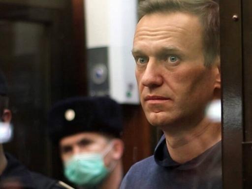 Alexei Nawalny während einer Gerichtsanhörung in Moskau am 2.2.2021. Ein Mann steht hinter einer Glasscheibe. Neben ihm stehen Polizisten.