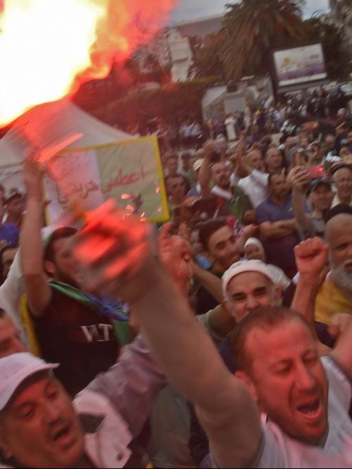 Demonstranten bilden Sprechchöre. Ein Mann im Vordergrund hält eine brennde Fackel in die Höhe.