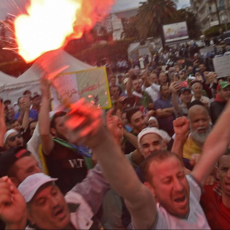 Demonstranten bilden Sprechchöre. Ein Mann im Vordergrund hält eine brennde Fackel in die Höhe. 