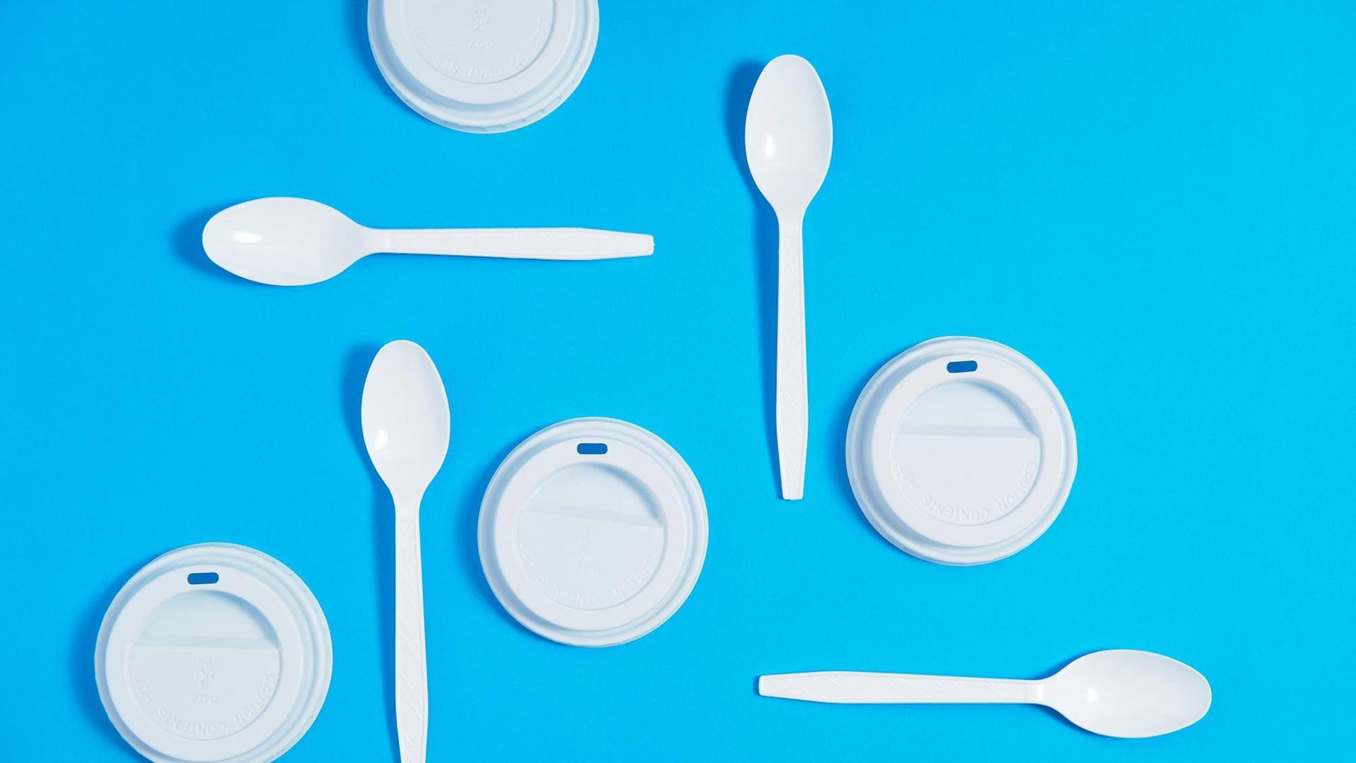 Plastikbesteck, bestehend aus Löffeln und Cafebecherdeckeln ordentlich angeordnet auf blauem Hintergrund. Plastikbesteck, bestehend aus Löffeln und Cafebecherdeckeln ordentlich angeordnet auf blauem Hintergrund.