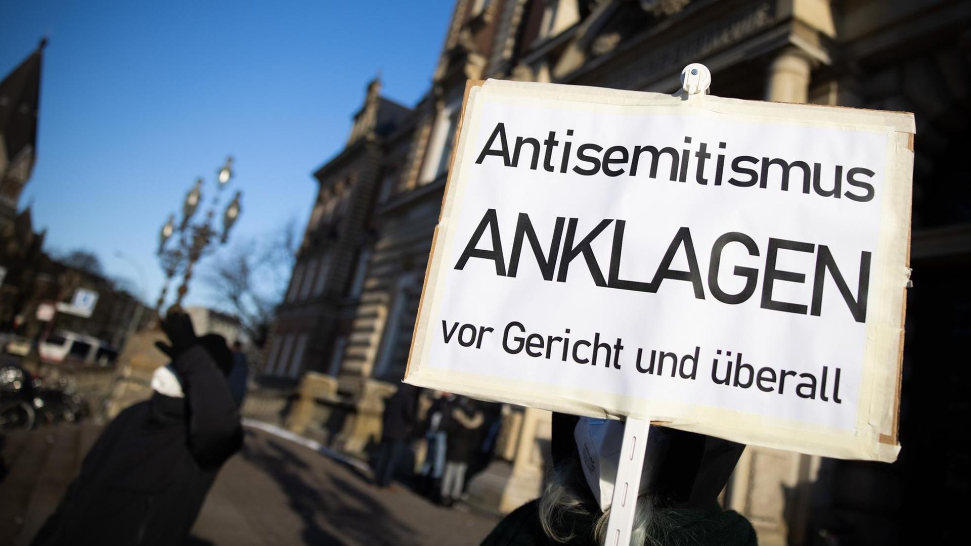 Eine Teilnehmerin einer Kundgebung hält eine Schild mit dem Text "Antisemitismus Anklagen vor Gericht und überall" vor dem Strafjustizgebäude in Hamburg Eine Teilnehmerin einer Kundgebung hält eine Schild mit dem Text "Antisemitismus Anklagen vor Gericht und überall" vor dem Strafjustizgebäude in Hamburg