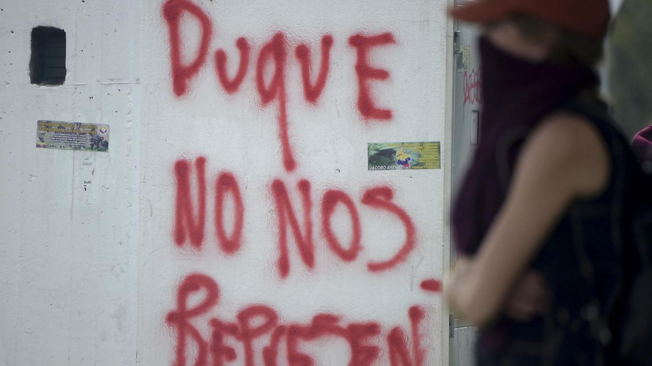 Demonstrant in Bogota neben einem Graffiti "Duque ist nicht unser Repräsentant" bei Zusammenstößen an der National-Universität in Bogota / AFP PHOTO / Raul Arboleda Demonstrant in Bogota neben einem Graffiti "Duque ist nicht unser Repräsentant" bei Zusammenstößen an der National-Universität in Bogota / AFP PHOTO / Raul Arboleda