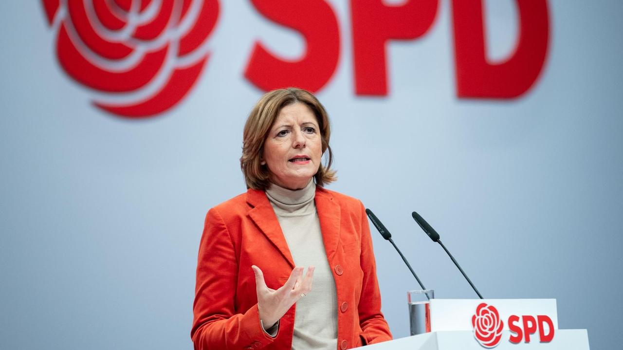 Malu Dreyer (SPD), steht beim SPD-Bundesparteitag in Berlin hinter einem rednerpult. Sie trägt einen roten Blazer. Im Hintergrund ist das Logo des Parteitags zu sehen: eine stilisierte Rose und der SPD-Schriftzug.