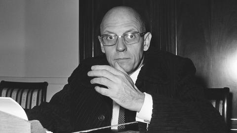 Michel Foucault sitzt an seinem Schreibtisch und schaut erstaunt in die Kamera. Aufgenommen in Paris 1970.