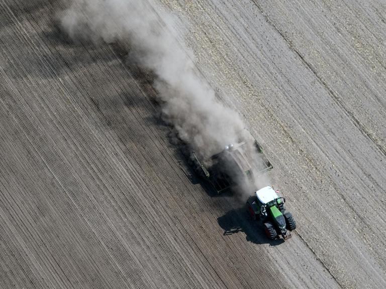 Eine dichte Staubwolke zieht ein Traktor bei Feldarbeiten in Schönhagen in Brandenburg hinter sich her, aufgenommen im August 2018