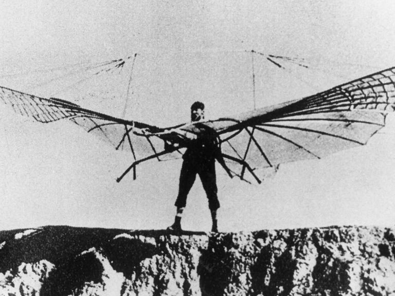 Otto Lilienthal bei einem seiner zahlreichen Gleitflugversuche. Er steht mit einem Gleitschirm auf vor einem Abhang