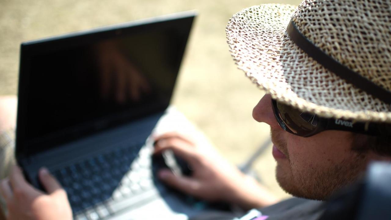 Ein Mann mit Strohhut, Sonnenbrille und Notebook auf dem Schoß Ein Mann mit Strohhut, Sonnenbrille und Notebook auf dem Schoß